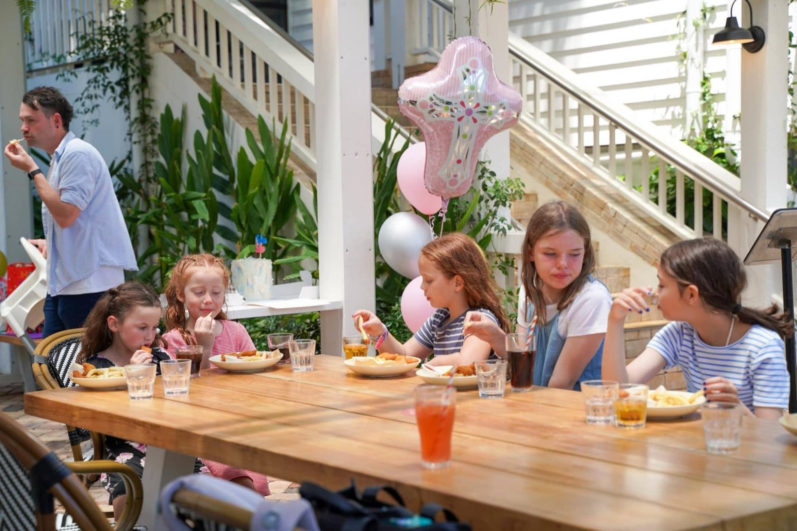 Children enjoying lunch together at a christening, with pink balloons overhead
